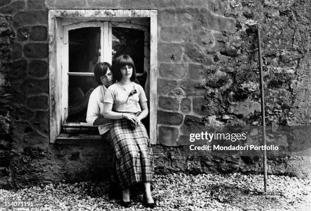 Jean Sorel, leaned on a windowsill, hugs his wife Anna Maria Ferrero, seated on his legs. Aulnay, 1970.