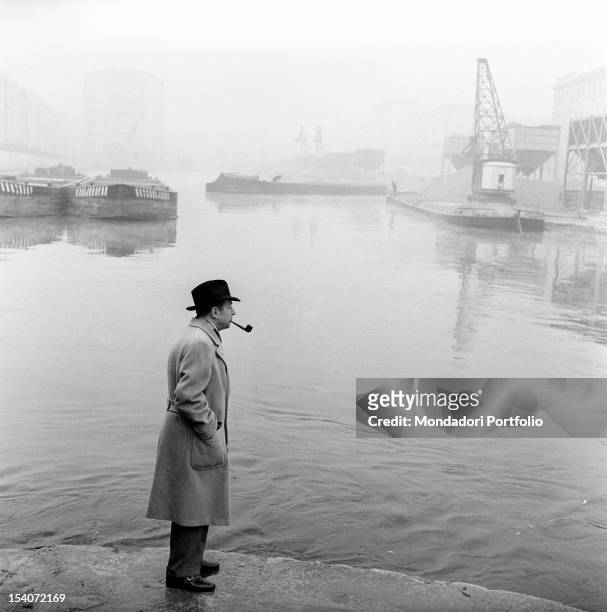 Belgian writer Georges Simenon smoking a pipe by the Navigli. Milan, 1950s