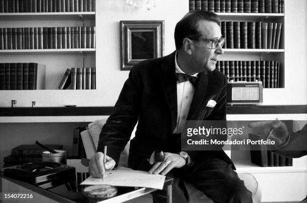 Belgian writer Georges Simenon wearing a dinner-jacket and writing. 1960s