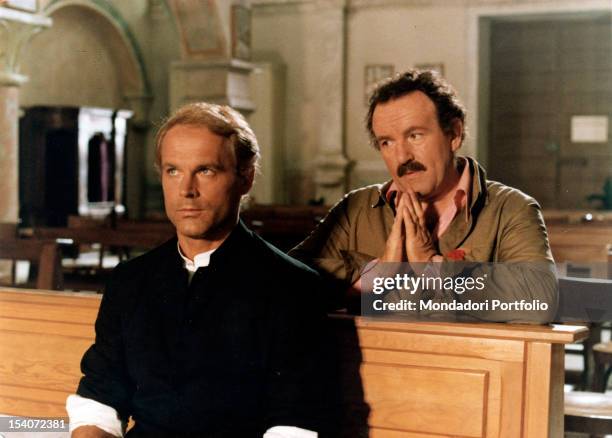 The Italian actor Terence Hill in the role of Don Camillo, sitting in a church. Behind him, the British actor Colin Blakely, in the role of Peppone,...