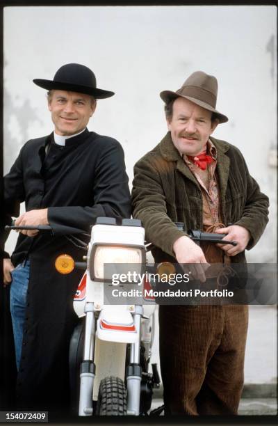The Italian actor Terence Hill in the role of Don Camillo and the British actor Colin Blakely in the role of Peppone, smiling and resting on the...