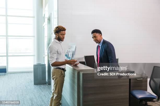 junger mann bringt kreditpapiere zu männlichem bankangestellten - bank teller and customer stock-fotos und bilder