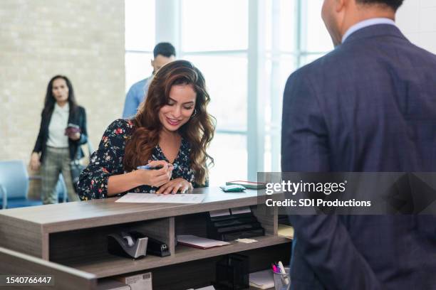 while unrecognizable male teller waits, woman fills out bank form - bank teller stock pictures, royalty-free photos & images