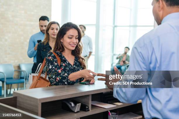 woman hands debit card to unrecognizable bank teller - bankpersoneel stockfoto's en -beelden