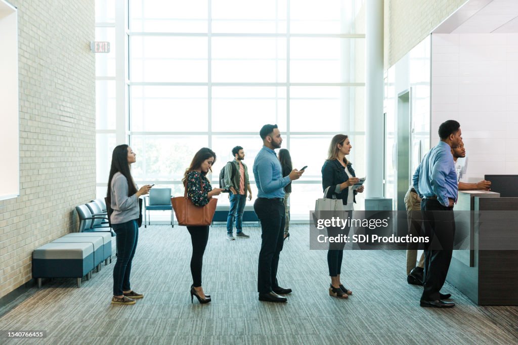 Customers with phones wait in line to see bank teller