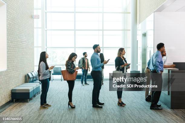 customers with phones wait in line to see bank teller - lining up imagens e fotografias de stock