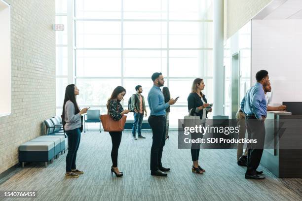 customers with phones wait in line to see bank teller - banco imagens e fotografias de stock