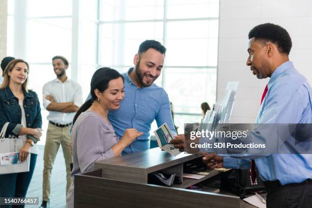 young couple smiles as male teller talks about savings options - bank teller stock pictures, royalty-free photos & images