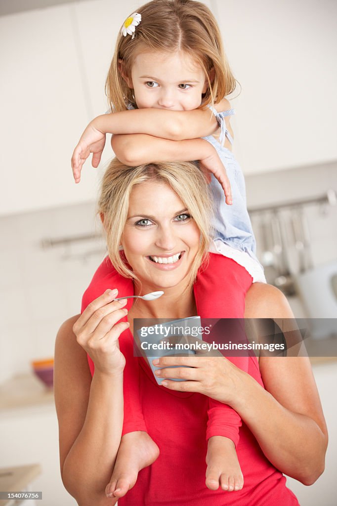 Tochter auf den Schultern sitzend während Mutter Essen Joghurt
