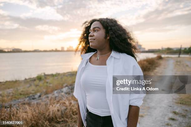 bipoc trans woman walks on levee - oversized necklace stock pictures, royalty-free photos & images