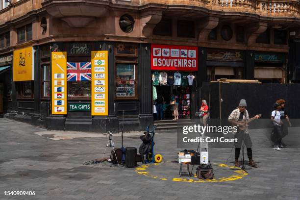 Busker plays outside a souvenir and vape shop in Leicester Square on July 18, 2023 in London, England. The proliferation of American-style candy...