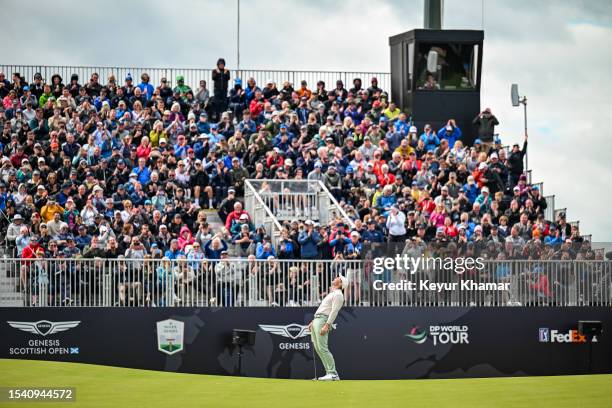 Rory McIlroy of Northern Ireland smiles after making a winning birdie putt on the 18th hole green while fans celebrate in the grandstand during the...