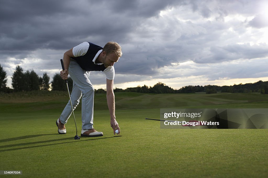 Man collecting golf ball from hole.