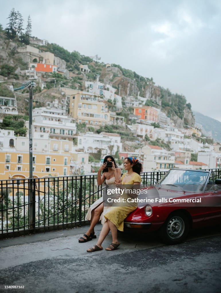 Two woman perch on a car bonnet in Positano, Italy