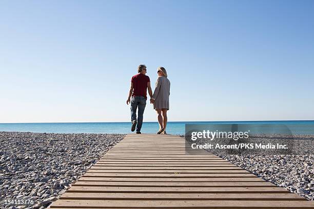 couple walk along boardwalk over pebble beach, sea - middlebare afstand stockfoto's en -beelden