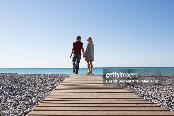 couple walk along boardwalk over pebble beach, sea - love on the rocks stock pictures, royalty-free photos & images