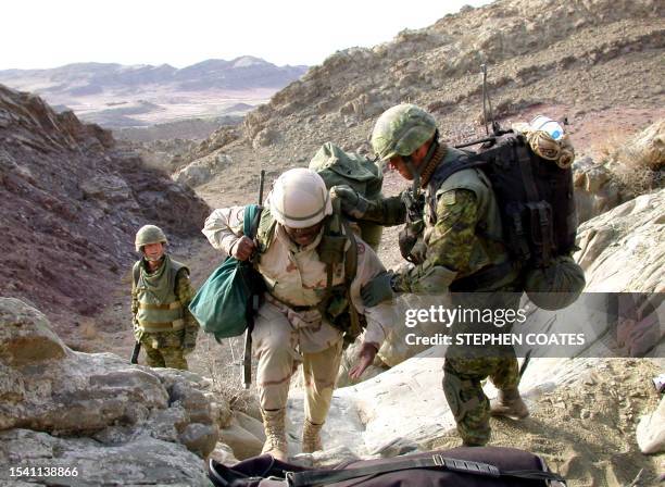 Canadian light infantry soldier helps a US soldier, 17 March 2002, in the rugged Arma mountains of eastern Afghanistan, where coalition forces have...