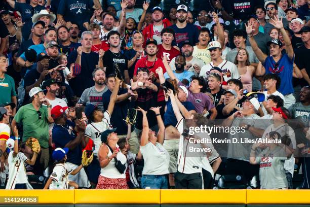 Fans try to catch a home run hit by Orlando Arcia of the Atlanta Braves during the fifth inning against the Arizona Diamondbacks at Truist Park on...