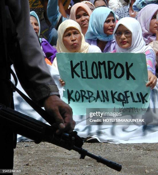 An Acehnese woman holds a placard reading "Group of conflict's victim" during a demonstration in Banda Aceh, 07 October 2002, while a policeman...