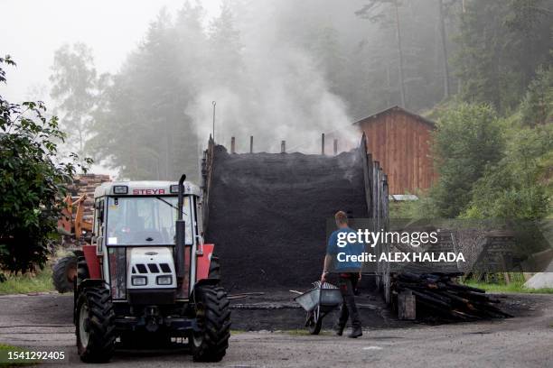 Intern Armin arrives with a wheelbarrow to collect charcoal from a pile in Rohr im Gebirge, Lower Austria, on July 18, 2023. Peter and his wife...