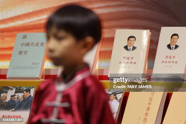 Boy wearing Chinese traditional clothes stands in front of a booth displaying Chinese President Xi Jinping's books at the 33rd Hong Kong Book Fair in...