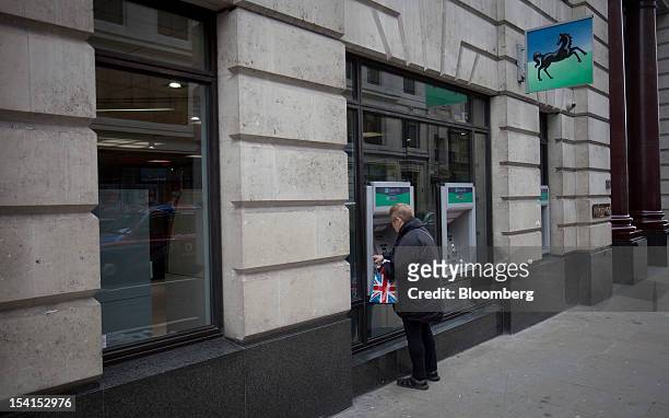 Customer holds a Union Jack bag as she uses an automated teller machine outside a Lloyds TSB bank branch, part of the Lloyds Banking Group Plc, in...