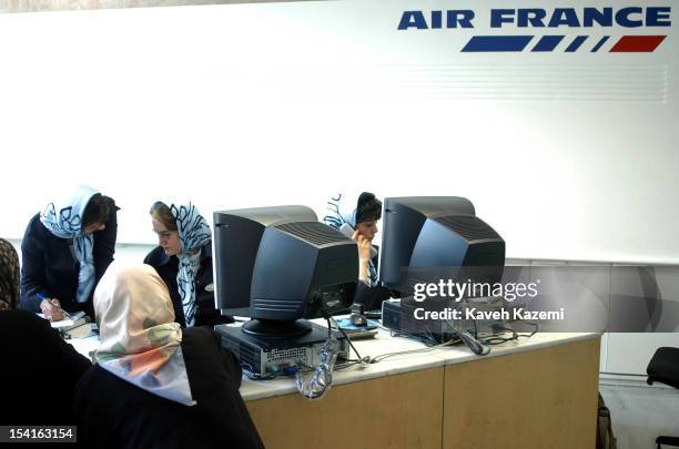Three Iranian women in headscarves work at the Air France desk after the airline resumed flight operations from Tehran, in mid-June 2004, after a...