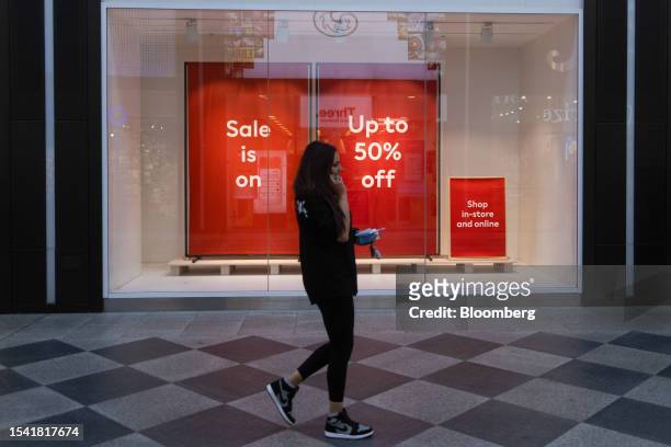 Shopper passes a clothing store advertising a discount sale in Oxford, UK, on Wednesday, July 19, 2023. Britain's inflation rate cooled more than...