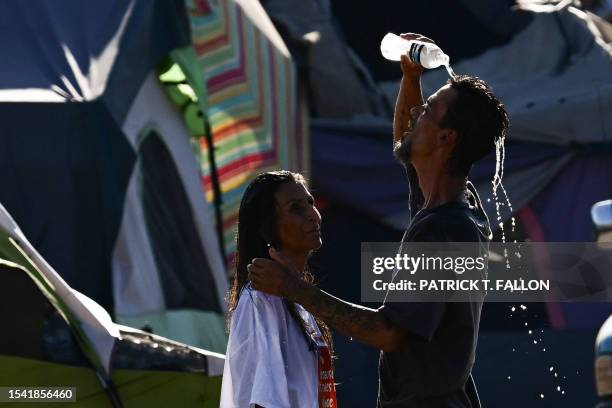 Roni and John pour water on themselves to cool off from extreme heat while residing in "The Zone," a vast homeless encampment where hundreds of...