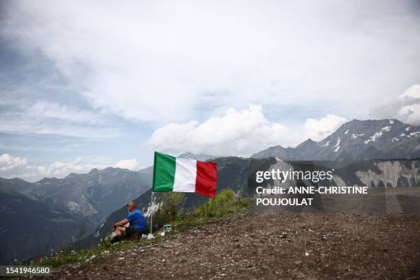 Man sits next to a fluttering Italian flag during the 17th stage of the 110th edition of the Tour de France cycling race, 166 km between...