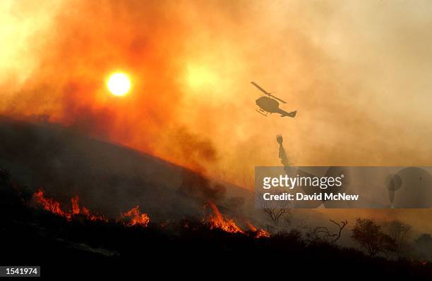 Helicopter drops water on a wildfire as the sun sets May 13, 2002 near Rancho Santa Margarita, CA. The fire consumed about 1,100 acres in less than...