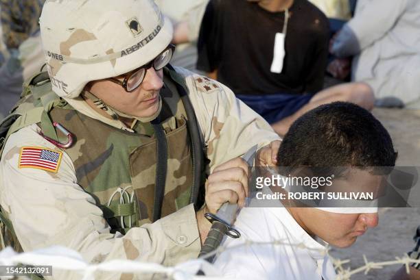 Specialist Mark Abbatiello of the 4th Infantry Division, 1st Brigade Combat Team 42 Field Artillery cuts the blindfold off a detainee 31 August 2003...
