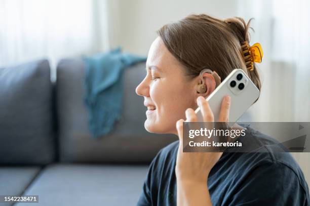 woman with hearing aid using smartphone - tecnología de asistencia fotografías e imágenes de stock