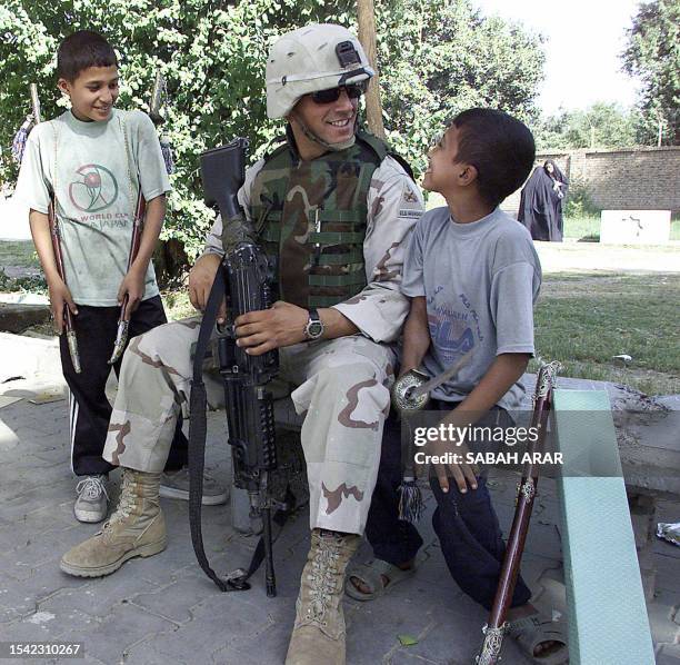 Soldier chats with Iraqi children selling plastic swords in Baghdad, 25 October 2003. Three US soldiers were wounded in an attack in the capital, a...