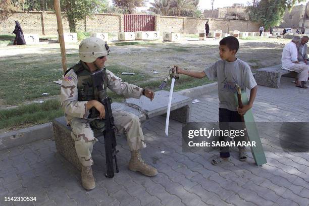 An Iraqi boy tries to sell a plastic sword to a US soldier in Baghdad, 25 October 2003. Three US soldiers were wounded in an attack in the capital, a...