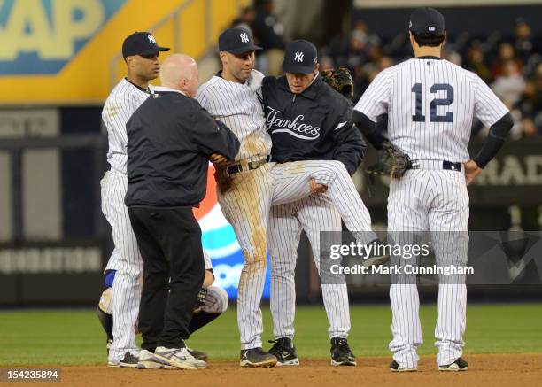 Derek Jeter of the New York Yankees is carried off the field by trainer Steve Donohue and manager Joe Girardi after Jeter fractured his left ankle in...