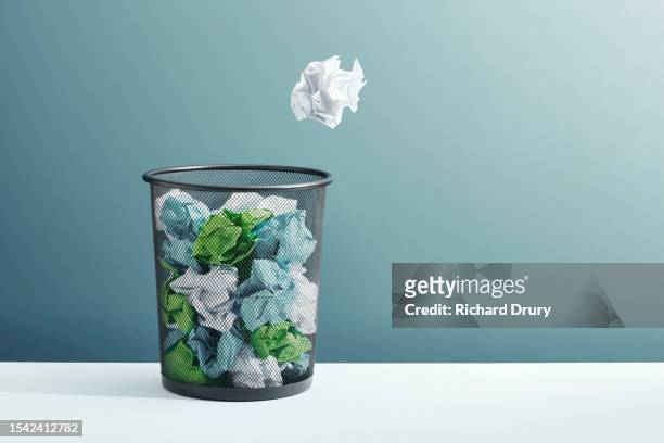 a ball of crumpled paper flying towards a full waste paper basket - afwijzing stockfoto's en -beelden