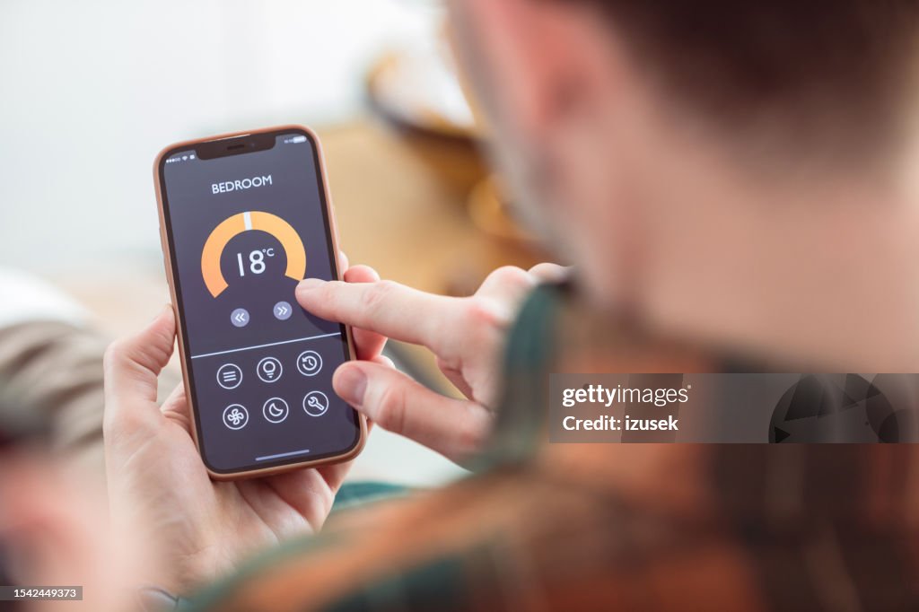 Mann, der Mobiltelefon benutzt, um Termostat zu Hause zu kontrollieren