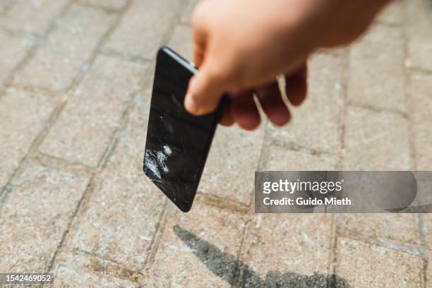 hand picking up cracked mobile phone of the ground outdoor. - cracked iphone stock pictures, royalty-free photos & images