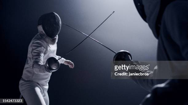 two professional fencers foil swords facing each other in combat with epic blue stage lighting and smoke effects. low angle view swords crossed - fechten stockfoto's en -beelden