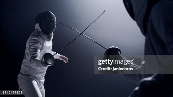 Two professional fencers foil swords facing each other in combat with epic blue stage lighting and smoke effects. Low angle view swords crossed