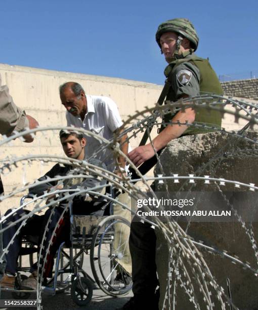 Handicapped Palestinian crosses a checkpoint as an Israeli soldier stands guard in the divided West Bank city of Hebron 29 May 2004. Israeli Prime...