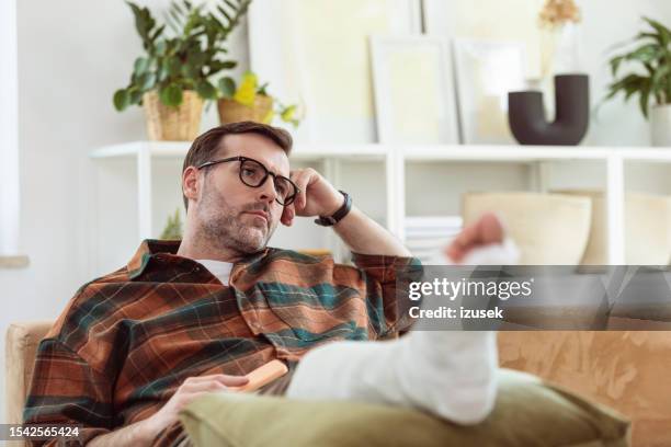 worried mature man with broken leg at home - gypsum stock pictures, royalty-free photos & images