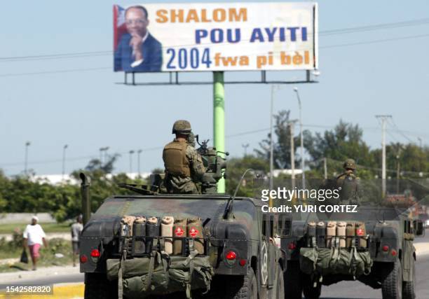 Marines in Humvees patrol Port Au Prince 03 March 2004, as they drive by an advertisment with a Jean Bertrand Aristide poster that says "Peace and...