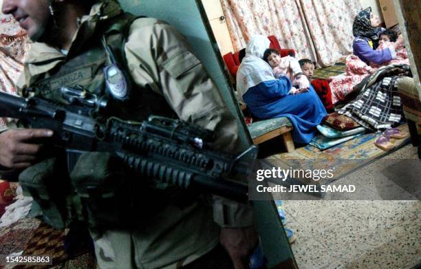 As Iraqi women sit with their babies in a room, US soldiers from the 1st Battalion, 22nd Regiment of the 4th Infantry Division searching their house...