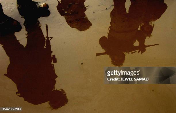 Soldiers from the 1st battalion, 22nd Regiment of the 4th Infantry Division are reflected in rain water on a flooded road in the former Iraqi...