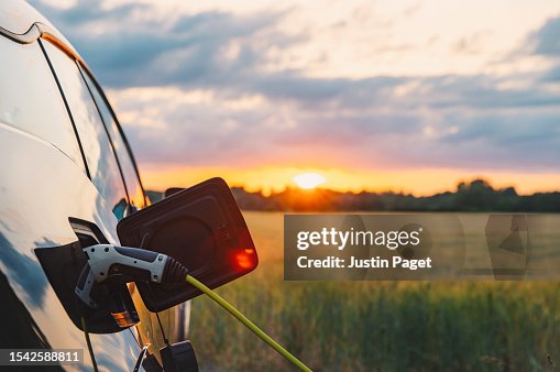 An electric car plugged in against a background of a rural location at sunset An electric car plugged in against a background of a rural location at sunset
