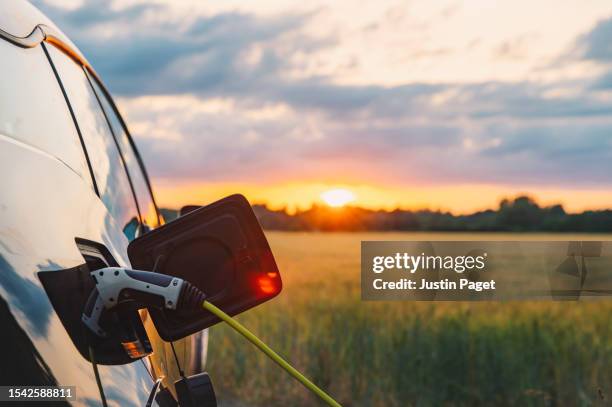 an electric car plugged in against a background of a rural location at sunset - power supply stock pictures, royalty-free photos & images