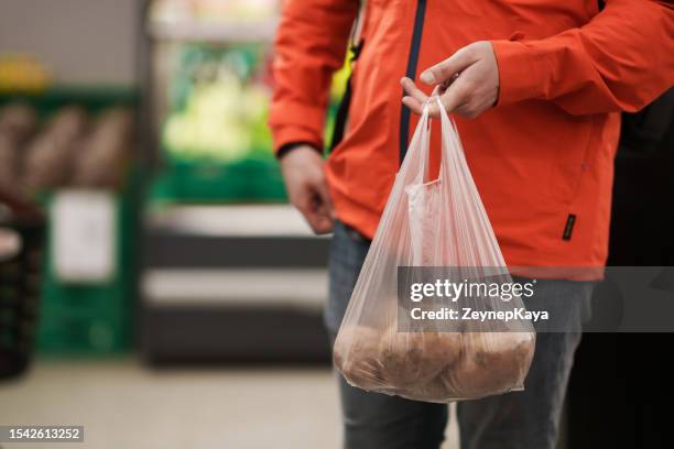 man holding a plastic bag full with potatoes in groceries store - plastic bag stock pictures, royalty-free photos & images