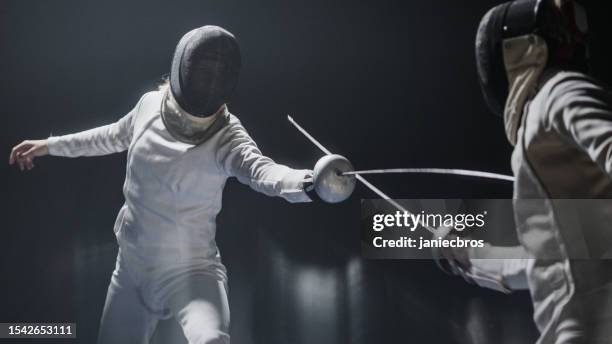two professional fencers foil swords facing each other in combat. lunging forward in offensive - fencing sport sword stock pictures, royalty-free photos & images